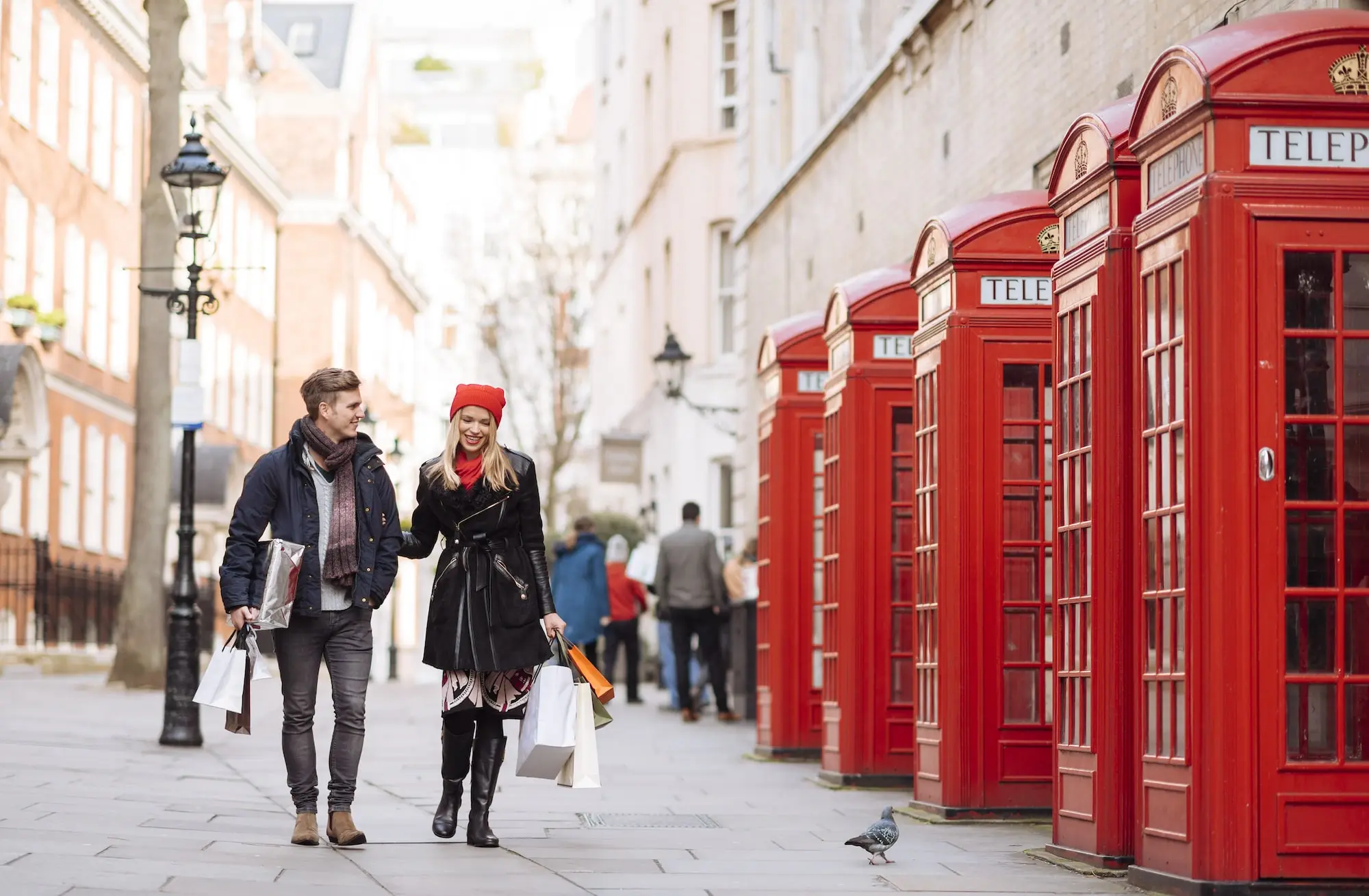 Photograph of man and woman walking arm in arm by several red phone booths in London.